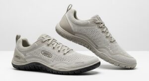 A pair of light grey Xero Shoes with mesh uppers, lace closures, and textured rubber soles. Engineered for walking, they offer all-day comfort with ventilation holes and a minimalistic style. The "Xero" brand name is displayed on the shoes.
