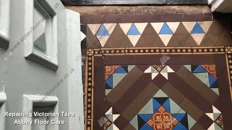 Repair work on loose Victorian hallway tiles affected by movement and dark grout contamination