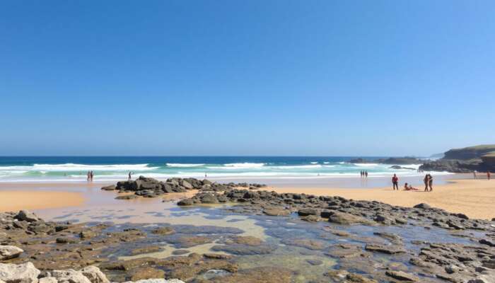 A sunny beach with clear waves, golden sands for sunbathing, rocky outcrops for exploration, accessible ramps, and a diverse array of people enjoying the day under a bright blue sky.